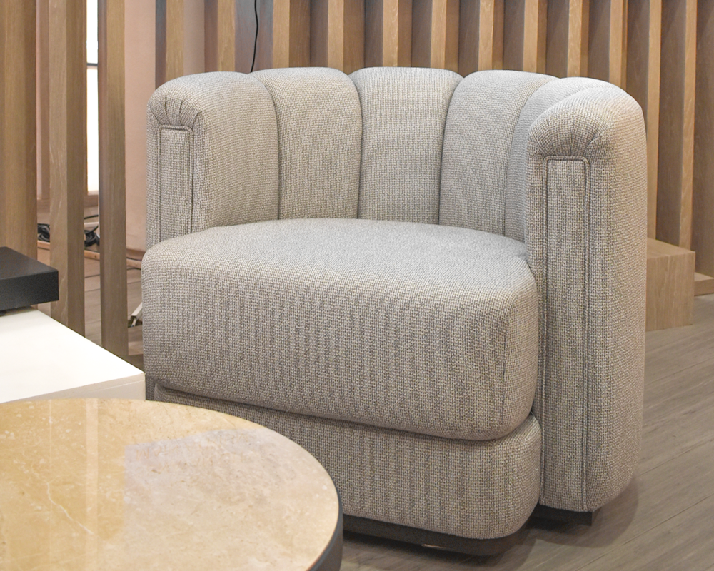 A Klaud Swivel Chair upholstered in textured light fabric, placed in a refined interior with complementary furniture.